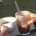 Ein Kakao im Glas und eine weisse Kaffeetasse, auf der Terrasse eines Cafés getrunken.