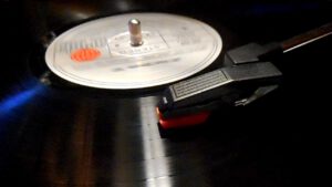 Bildausschnitt einer Vinyl-Platte mit weißem Aufkleber in der Mitte und schwarzem Tonkopf auf der rechten Seite.